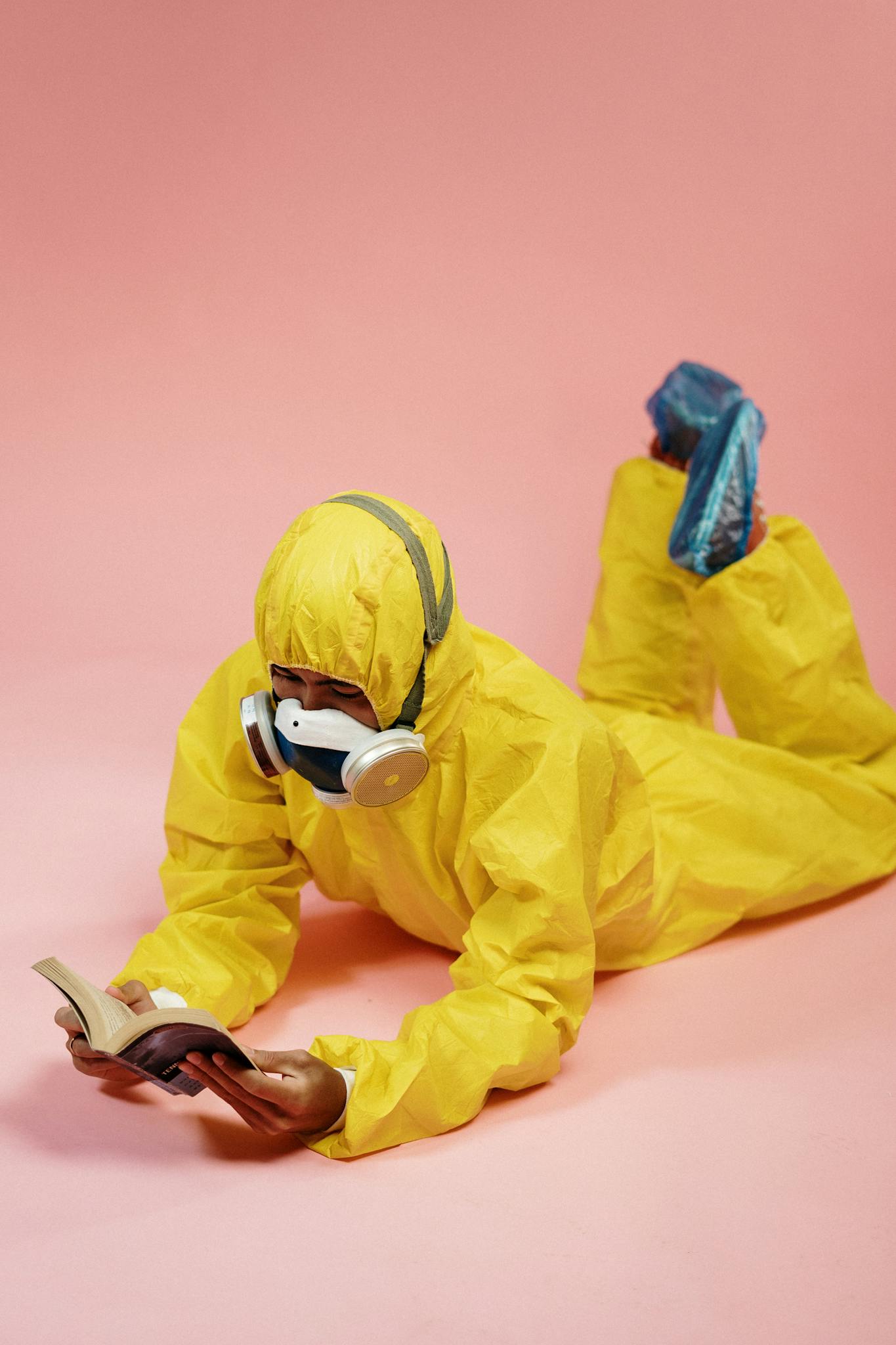 Adult in a yellow hazmat suit reading indoors, combining safety and leisure.